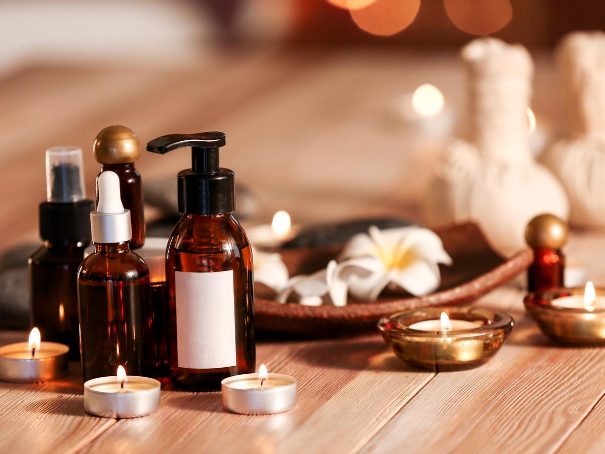 Massageöle und brennende Teelichter auf einem Holztisch.